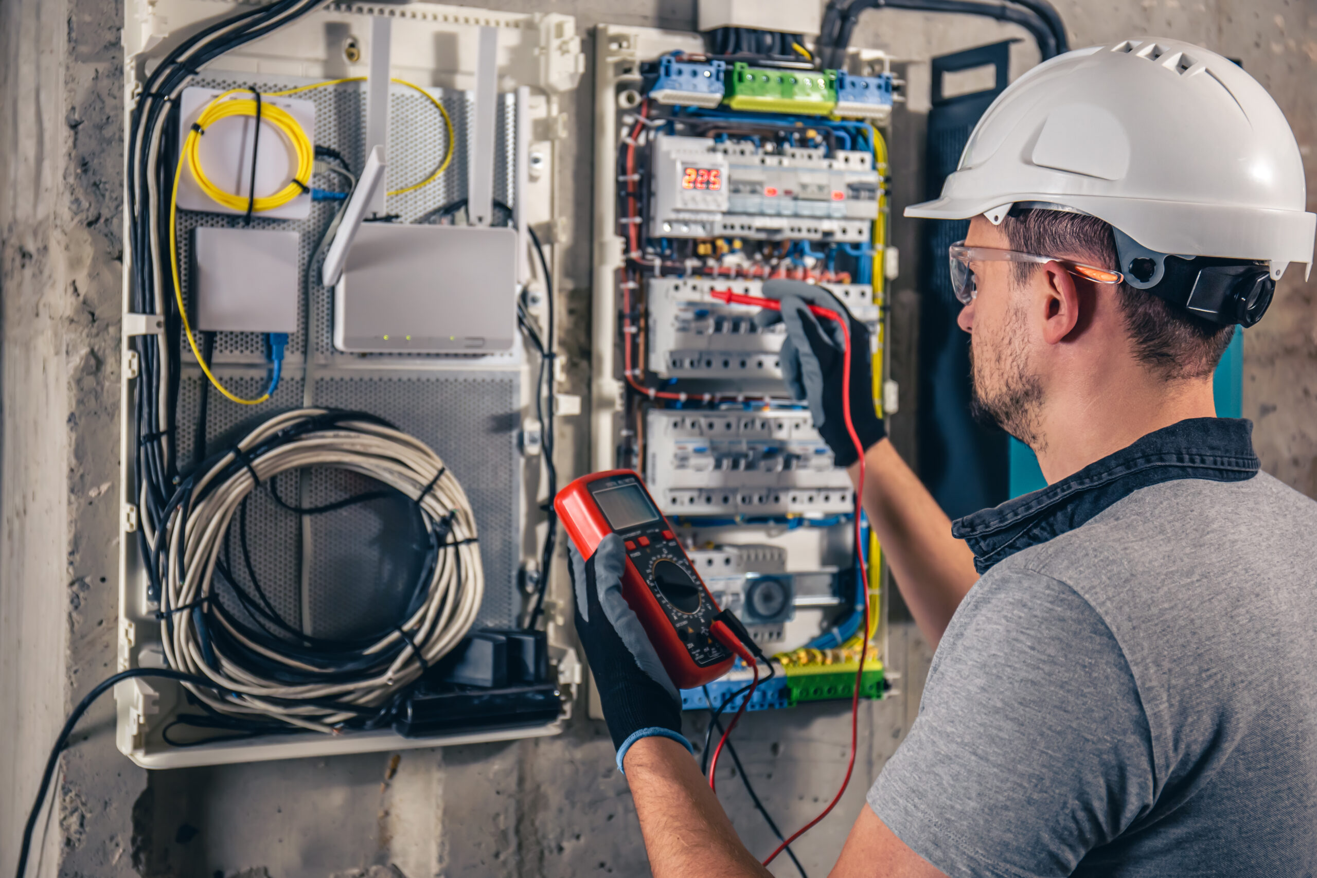 Man, an electrical technician working in a switchboard with fuses. Man, an electrical technician working in a switchboard with fuses. Installation and connection of electrical equipment. Professional uses a tablet.